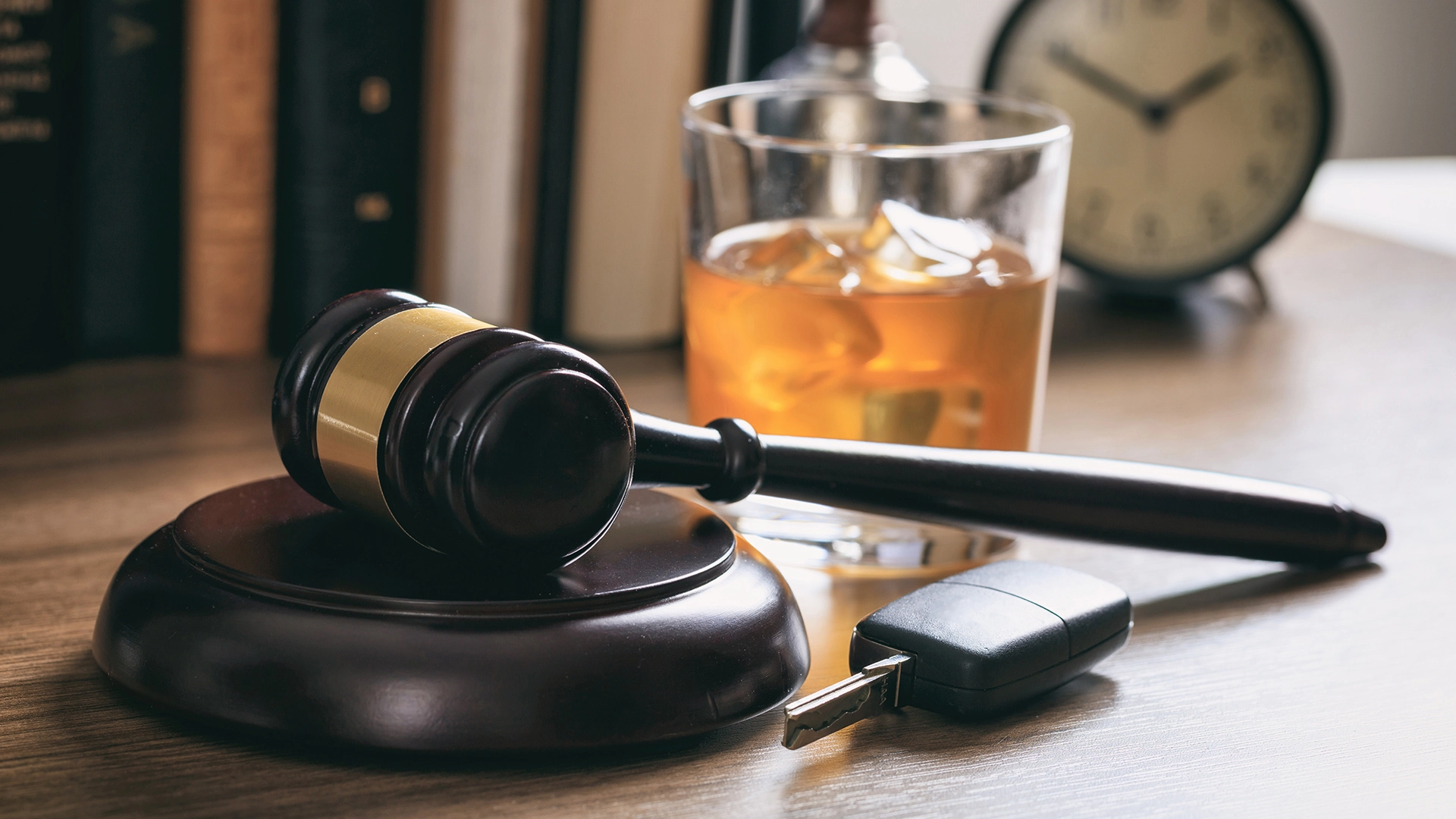 A gavel, whiskey glass, and car keys on a table representing a DUI or DWI charge