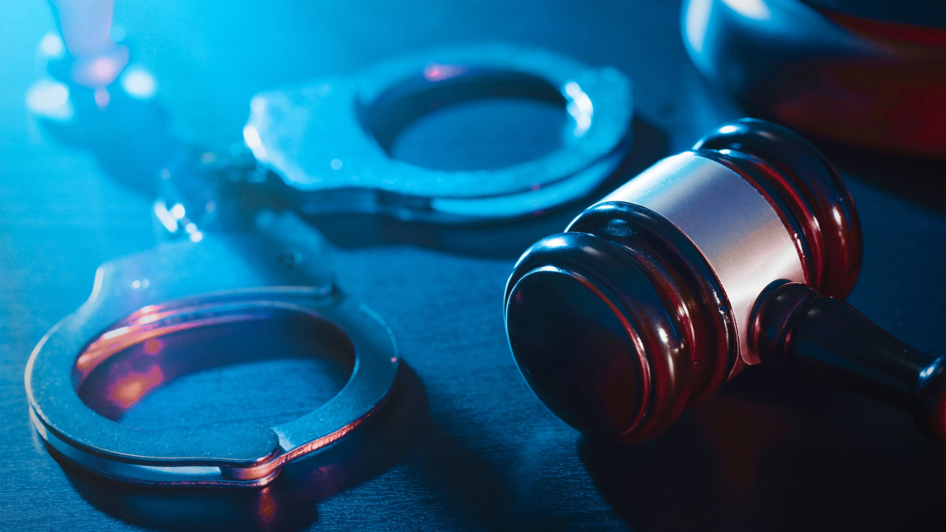 A pair of handcuffs and a gavel with blue light representing the repercussions of a sexual crime
